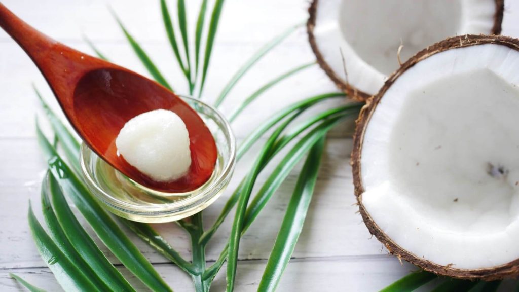 A whole coconut positioned next to a jar of creamy coconut oil, highlighting the source of this nourishing product.